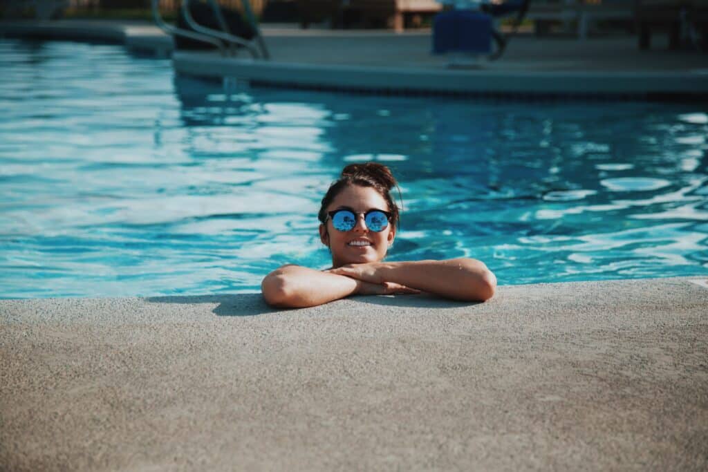 Mulher de óculos escuro, sorrindo na beira da piscina