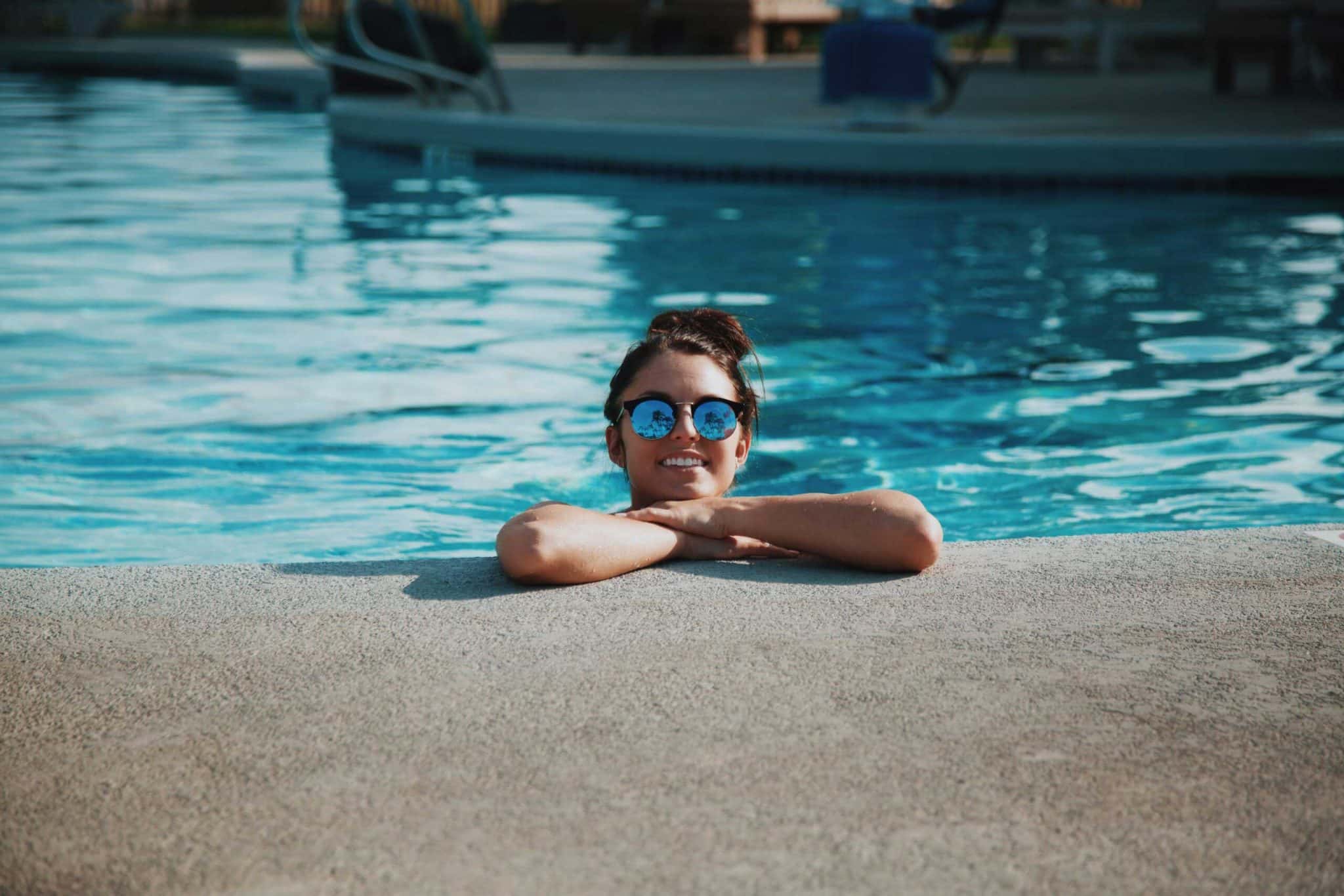 Woman in sunglasses smiling at poolside